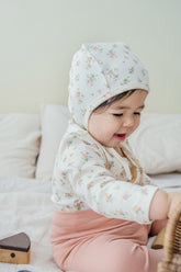 Baby wearing the Cream Floral bodysuit while seated and playing – highlighting the soft cotton fabric and adorable bonnet design